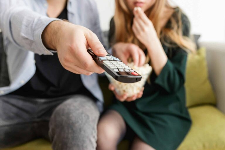 A couple on a couch with a TV remote and popcorn, the kind of household viewers the Disney+ Vidio bundle targets