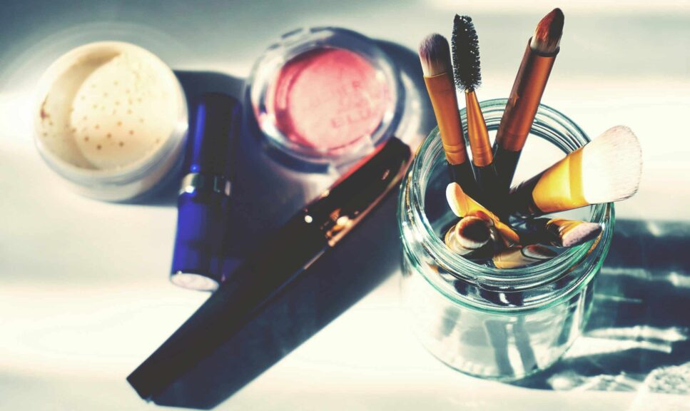 Artistic flat lay of makeup brushes in a jar surrounded by colorful cosmetics, perfect for beauty themes. June beauty launches