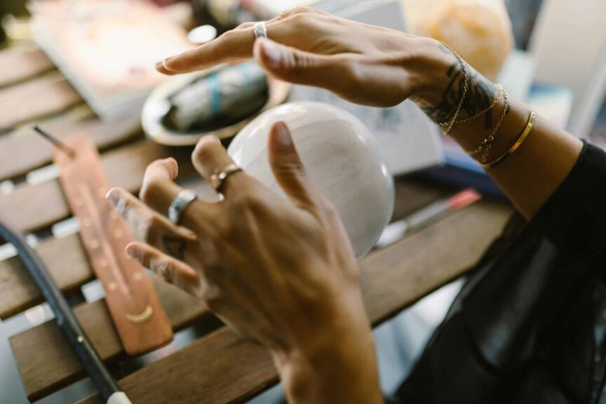 A close-up of hands with jewelry interacting with a mystical crystal ball on a wooden table. spirituality, new moon, new moon in cancer