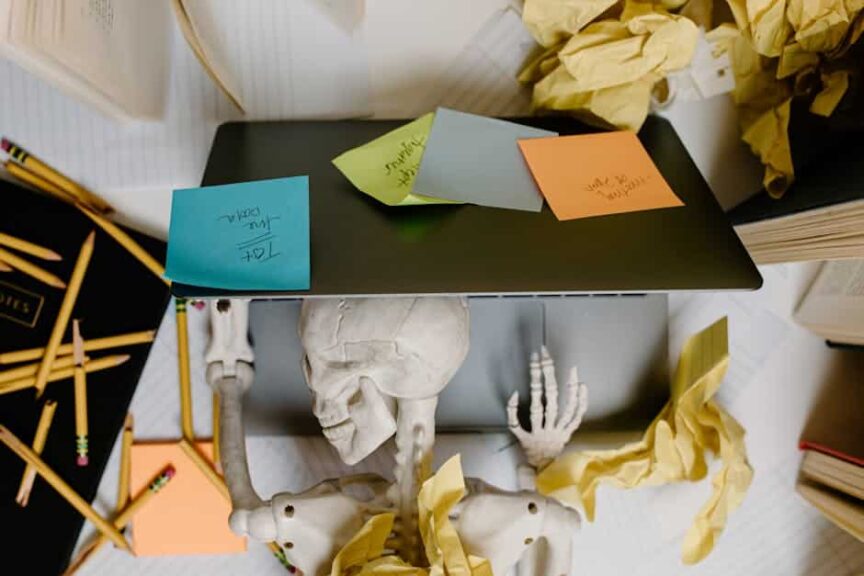 Skeleton at a laptop surrounded by notes and paper, symbolizing work burnout and the need for a digital detox.