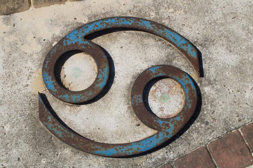 Close-up of a rusted Cancer zodiac symbol on a concrete wall. Venus in Cancer
