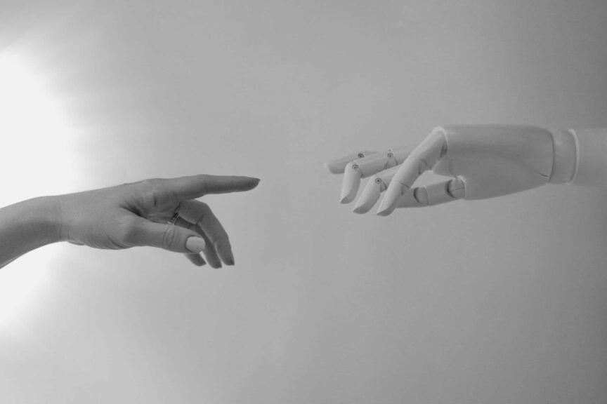 Black and white image of a human hand and a robotic hand reaching toward each other, symbolizing the connection between AI and love. Image by Tara Winstead via Pexels.
