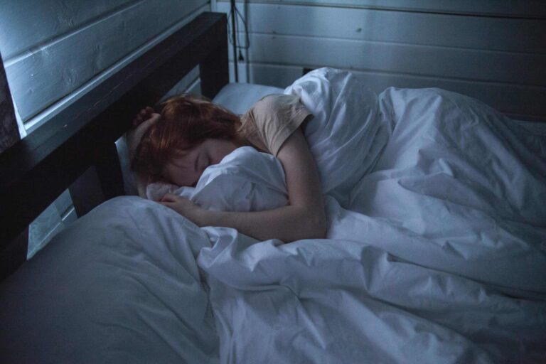 A woman sleeping peacefully in a cozy bedroom, enveloped by soft white sheets, under the gentle glow of night lighting. sleep supplements