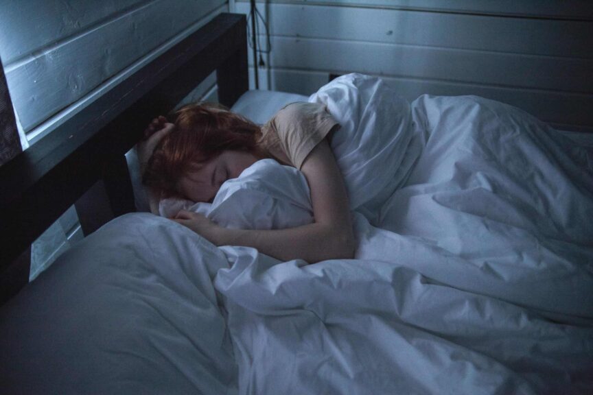 A woman sleeping peacefully in a cozy bedroom, enveloped by soft white sheets, under the gentle glow of night lighting. sleep supplements