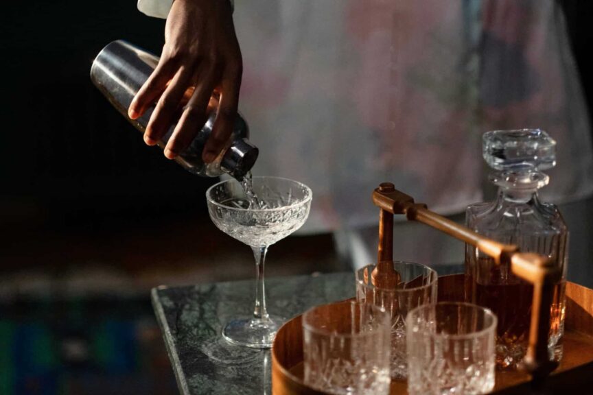 A bartender pours a cocktail into a glass from a shaker, set in a cozy home bar.