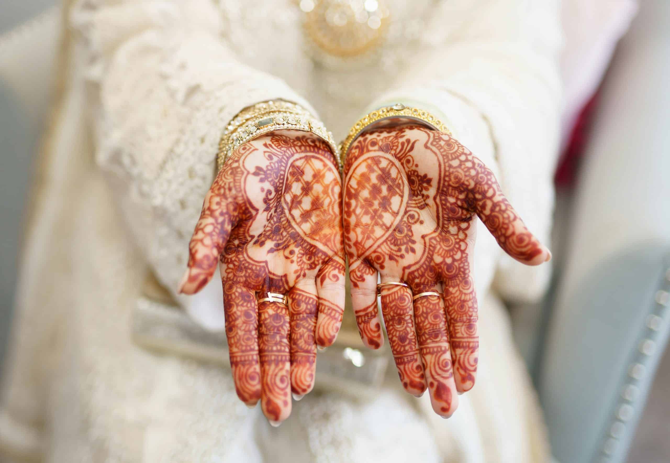 Beautiful bridal henna tattoo with heart design on outstretched hands wearing traditional attire. Wedding beauty ritual