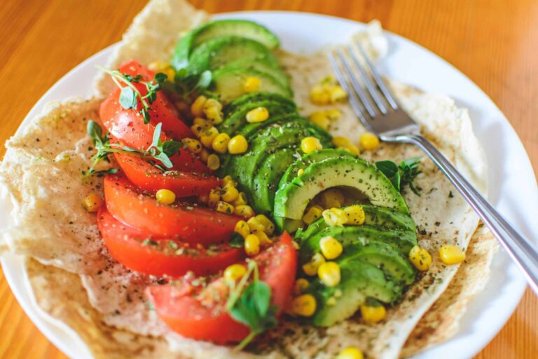 A vibrant salad vegan meals with avocado, tomato, and corn on flatbread, topped with herbs, perfect for a healthy meal.