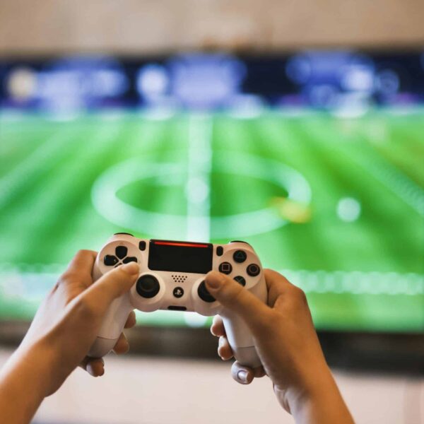 Close-up of hands holding a game controller playing a football video game on screen. platinum