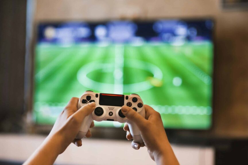 Close-up of hands holding a game controller playing a football video game on screen. platinum