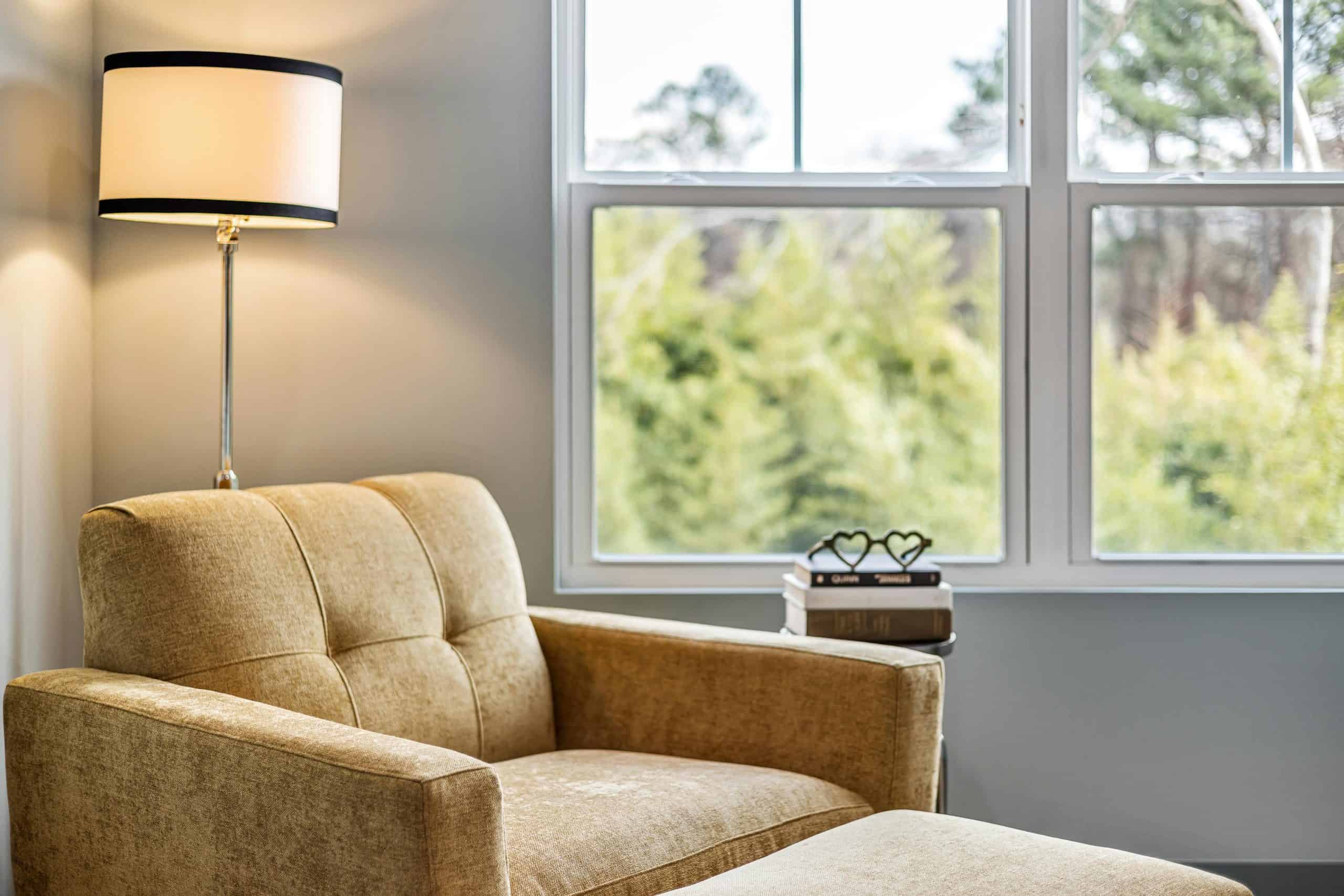 Modern living room with cozy armchair, footstool, and large window view. home sanctuary