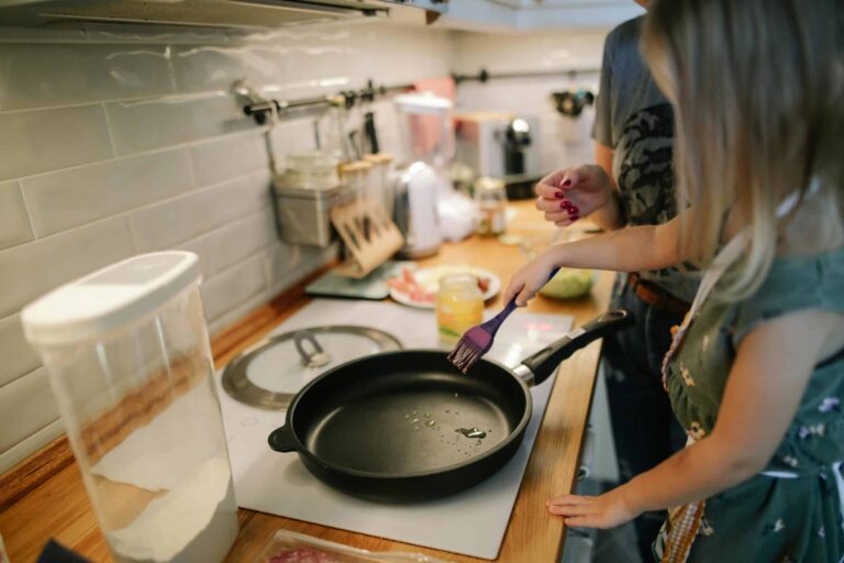 Young girl cooking with a frying pan under adult supervision in a modern kitchen. kitchen gadgets