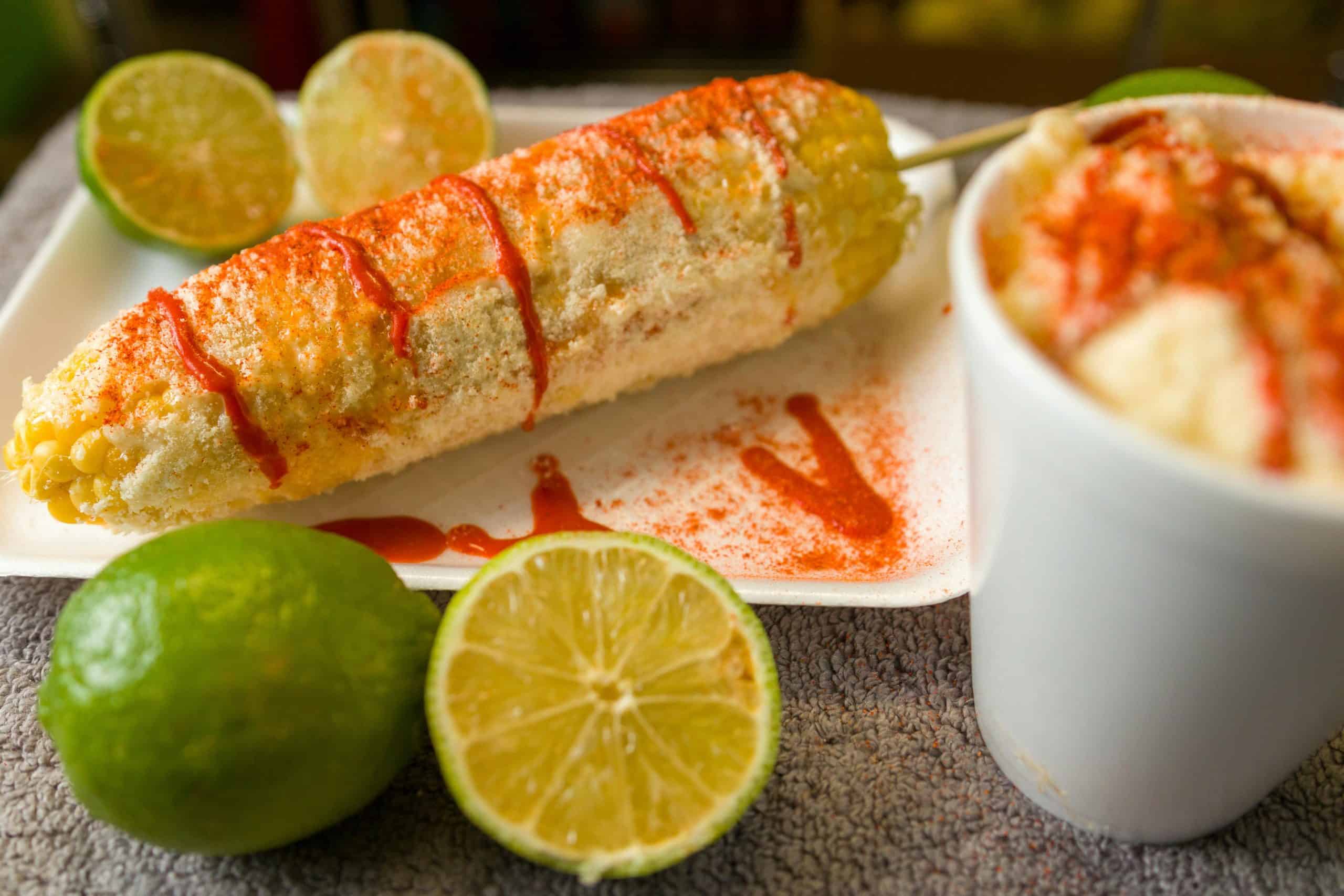 Close-up of Mexican elote topped with cheese and chili powder served with fresh lime.