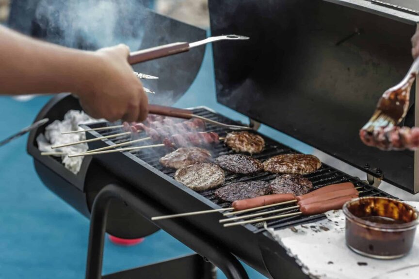 Delicious meats and sausages grilling on a barbecue outside, perfect for a summer picnic. 2-zone grilling