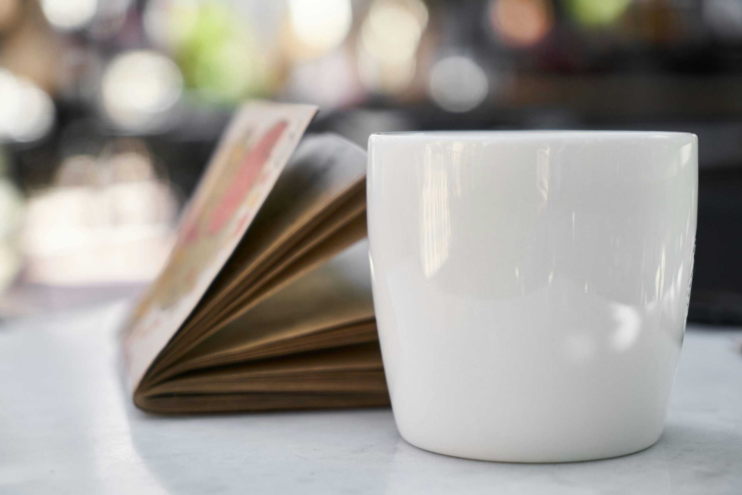 A white mug of coffee beside an open book on a marble table, indoors. home sanctuary