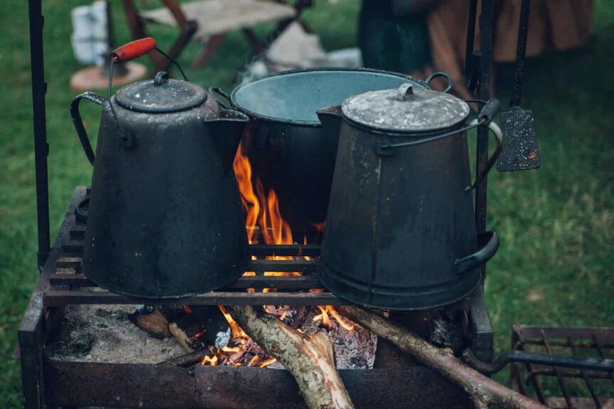 Camp kettles and pot over open fire at an outdoor campsite, ideal for rustic cooking themes. Portable cooking gear for camping