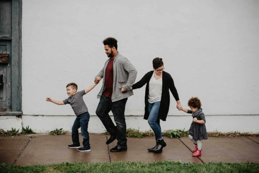 A joyful family walking together outdoors, holding hands in a playful and happy moment. Final days of summer.