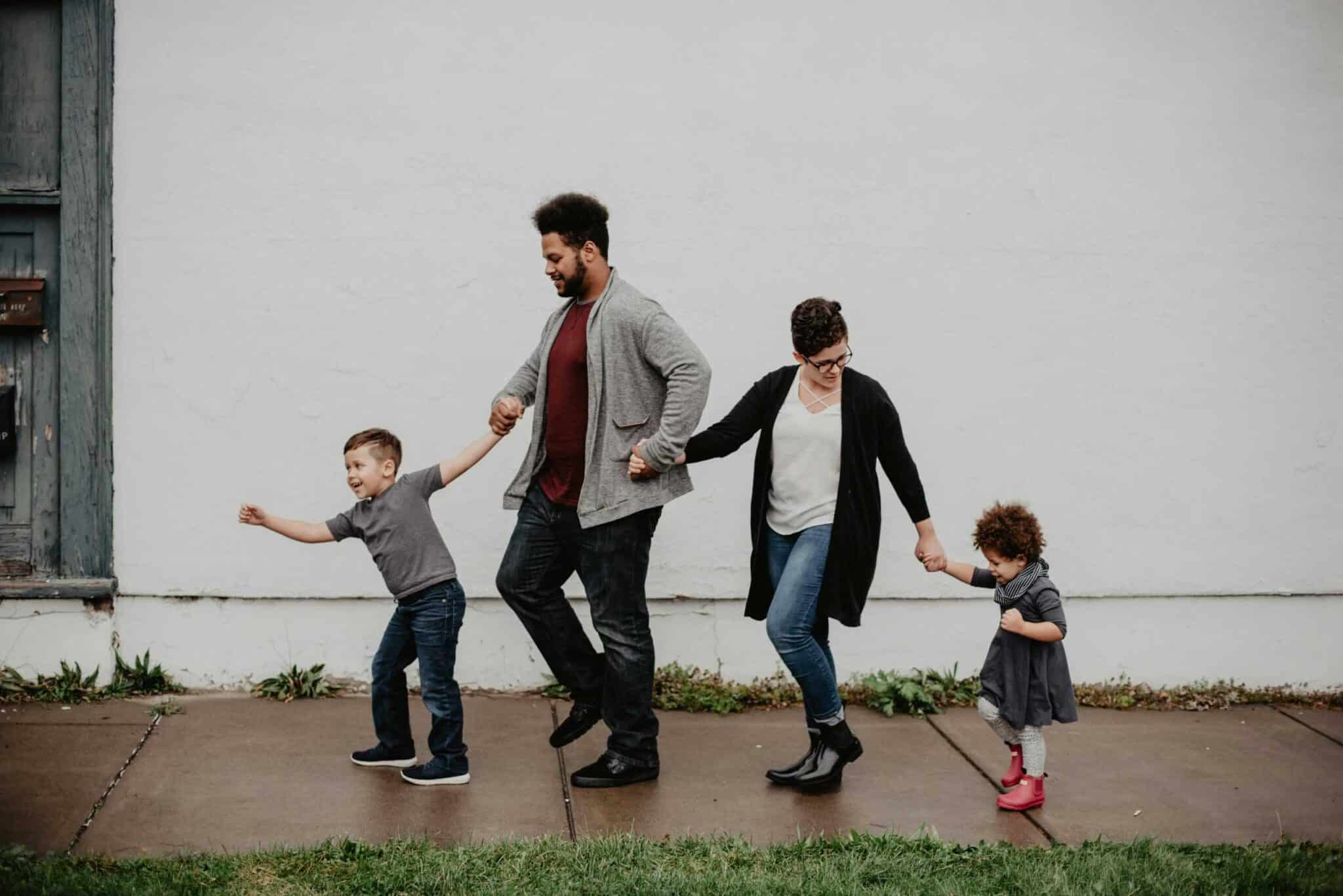 A joyful family walking together outdoors, holding hands in a playful and happy moment. Final days of summer.