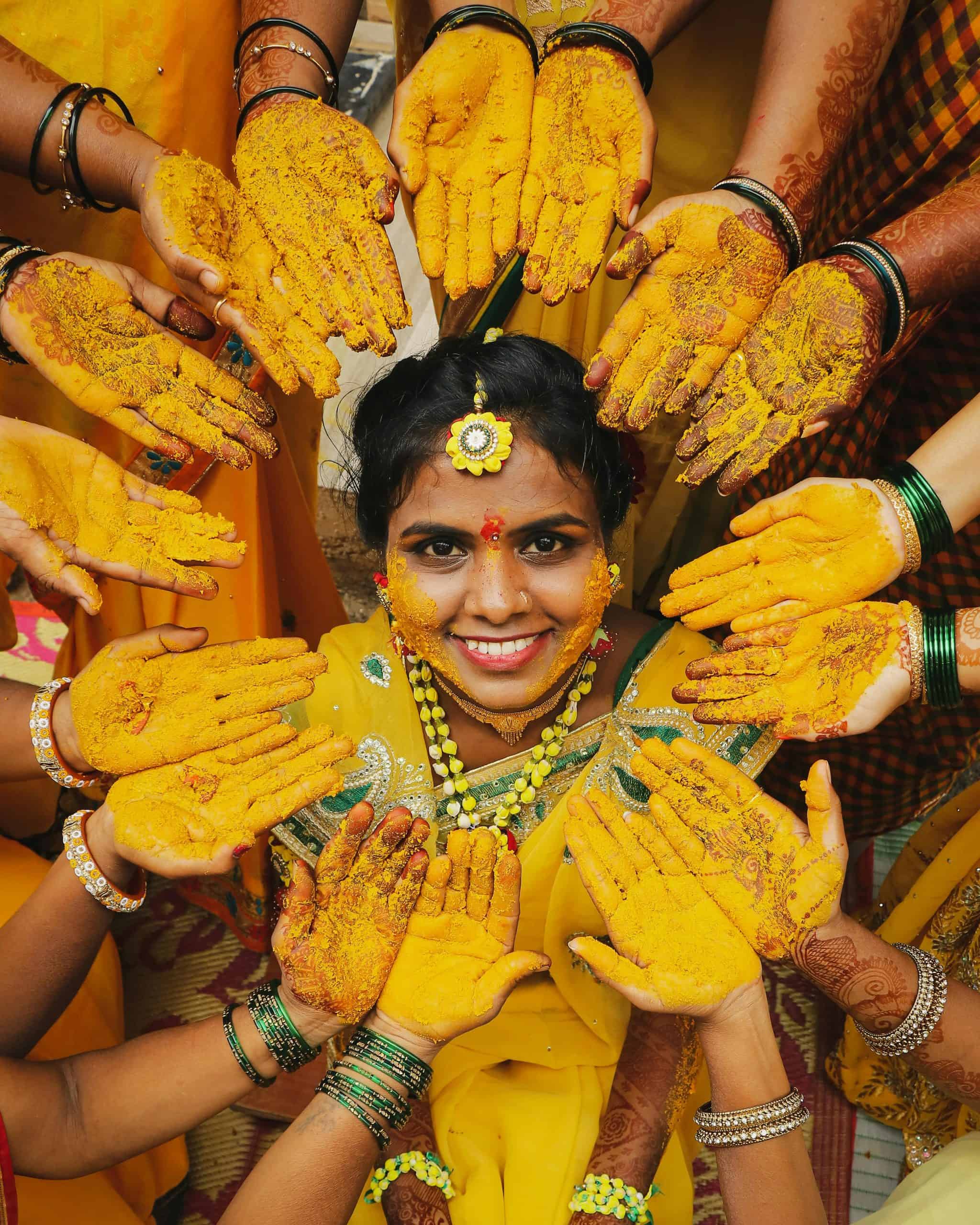 Cheerful bride surrounded by turmeric-covered hands during a vibrant traditional Haldi ceremony. Wedding beauty ritual
