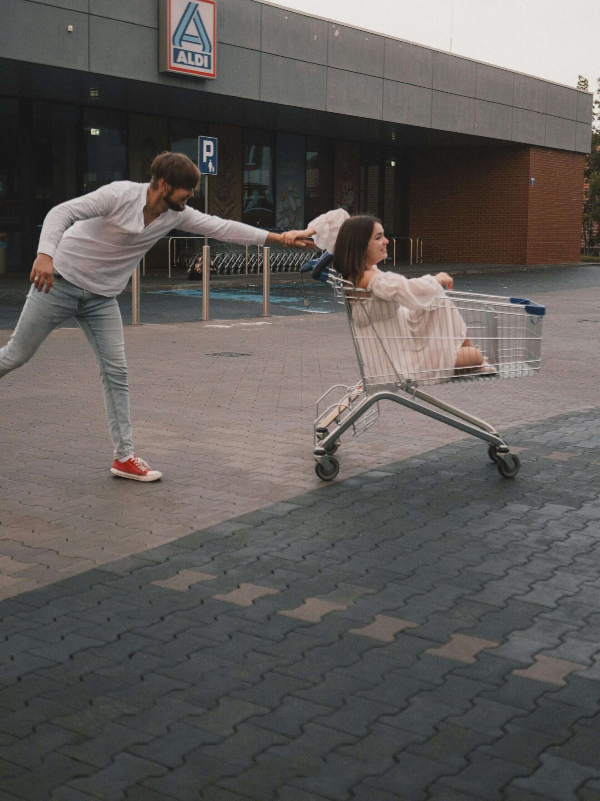 A joyful moment of a couple playing with a shopping cart outside a store.