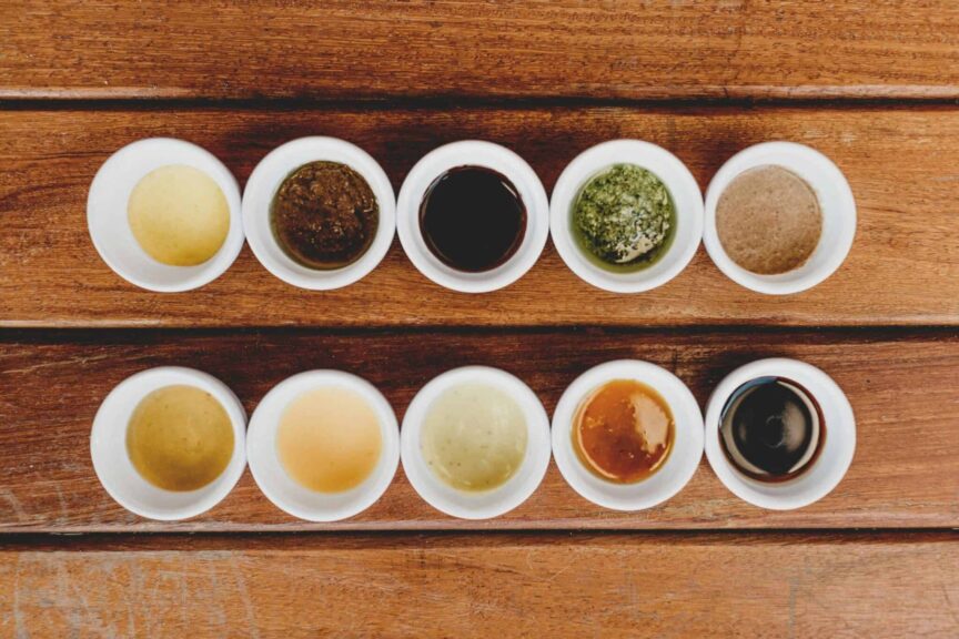 Assorted sauces and condiments displayed in bowls on a rustic wooden table.