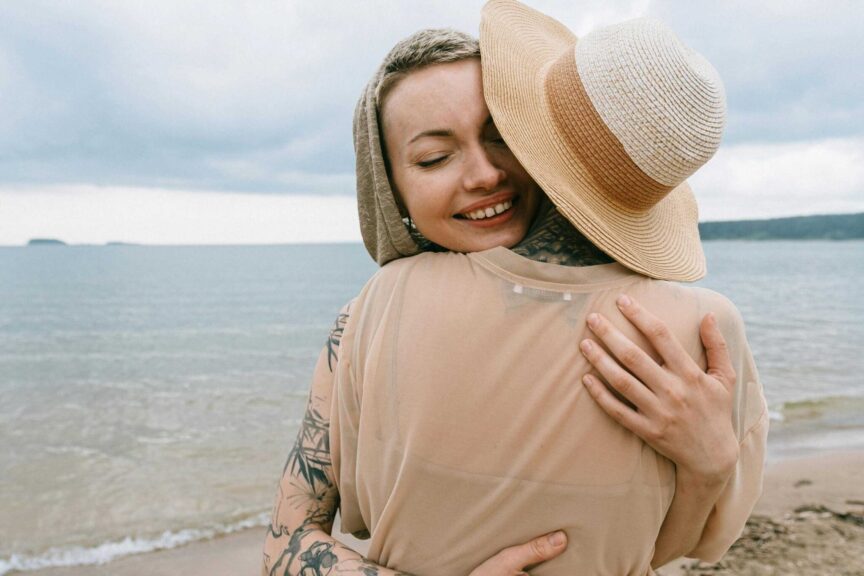 Two women embracing on a serene beach, expressing joy and friendship. Daily devotional