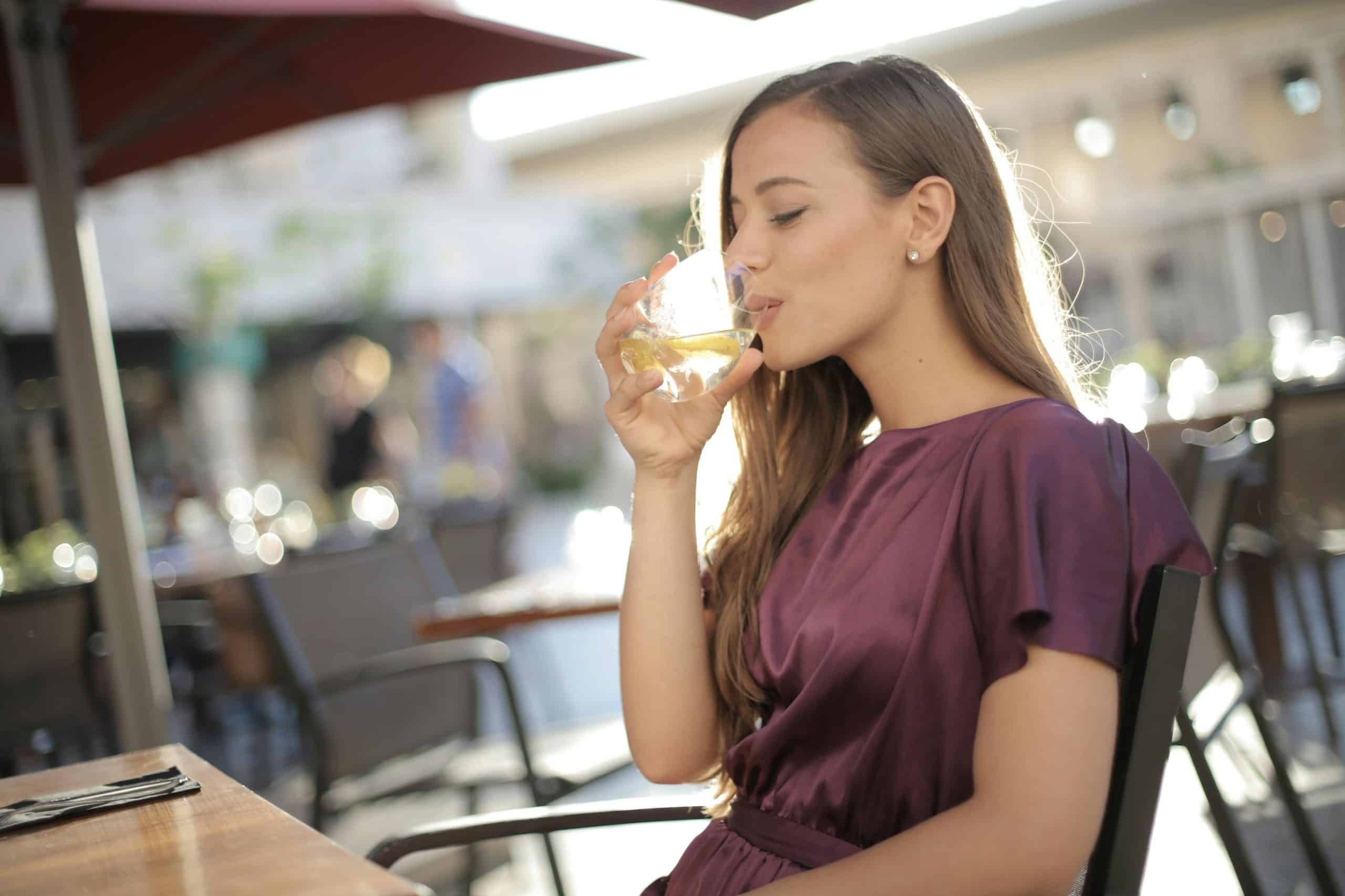 A woman in a purple top enjoys a refreshing drink outdoors, capturing a moment of relaxation.