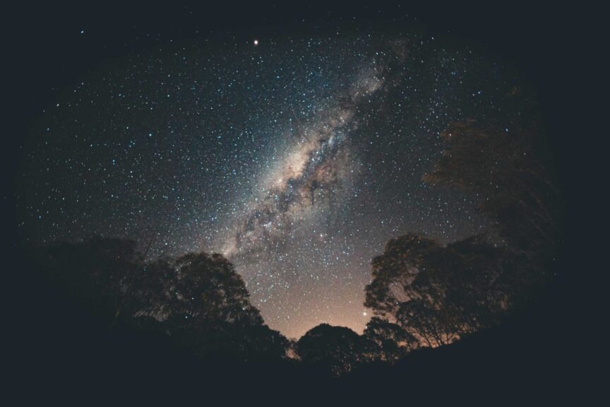Stunning view of the Milky Way galaxy over silhouetted trees in a tranquil night setting. Ceres Retrograde