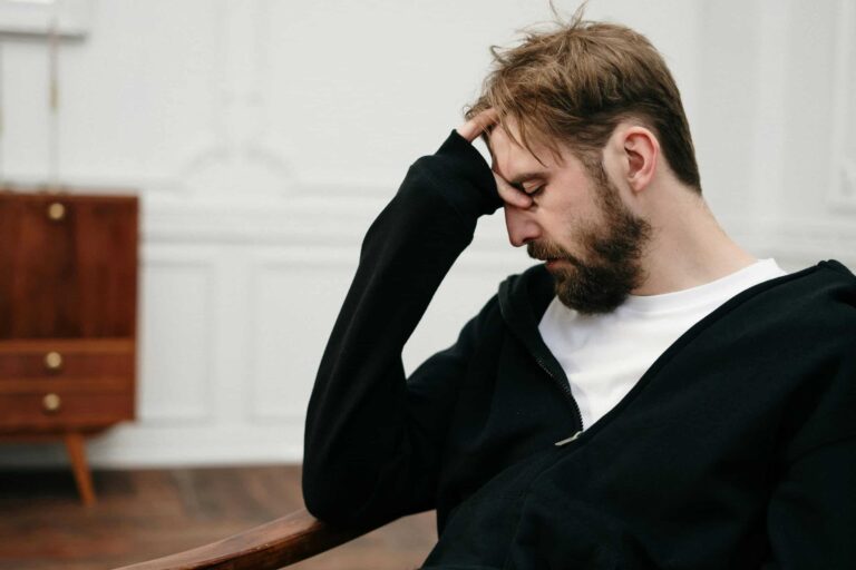 A man sits pensively with his hand on his face, capturing a moment of introspection and stress, sabotaging, relationship