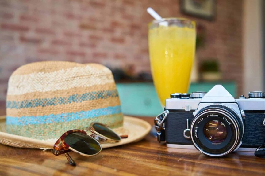 A stylish scene showcasing a vintage camera, hat, and orange juice, evoking summer travel vibes. Multi-generational travel trip