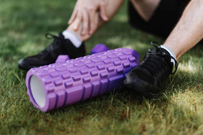 Black sneakers and purple foam roller on grass, outdoor fitness scene. Sore Muscle Recovery