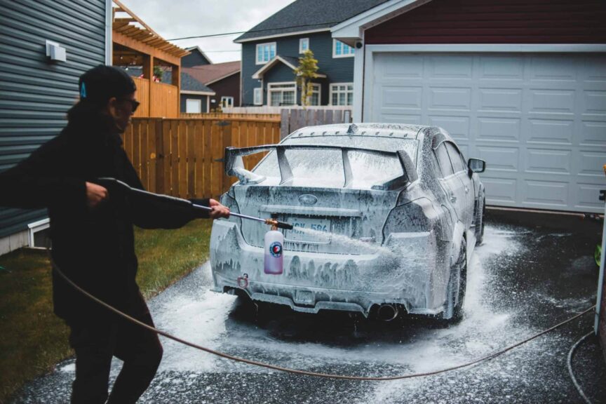 Side view of faceless male in black clothing washing car with foam in yard of house in daytime. Pressure Washer Recall