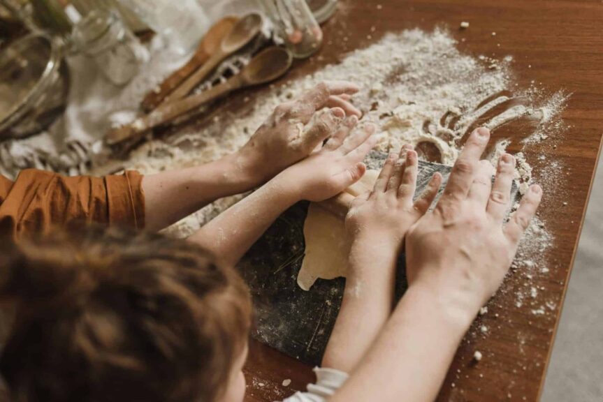 A parent and child bonding while kneading dough in a messy kitchen environment. bake with kids