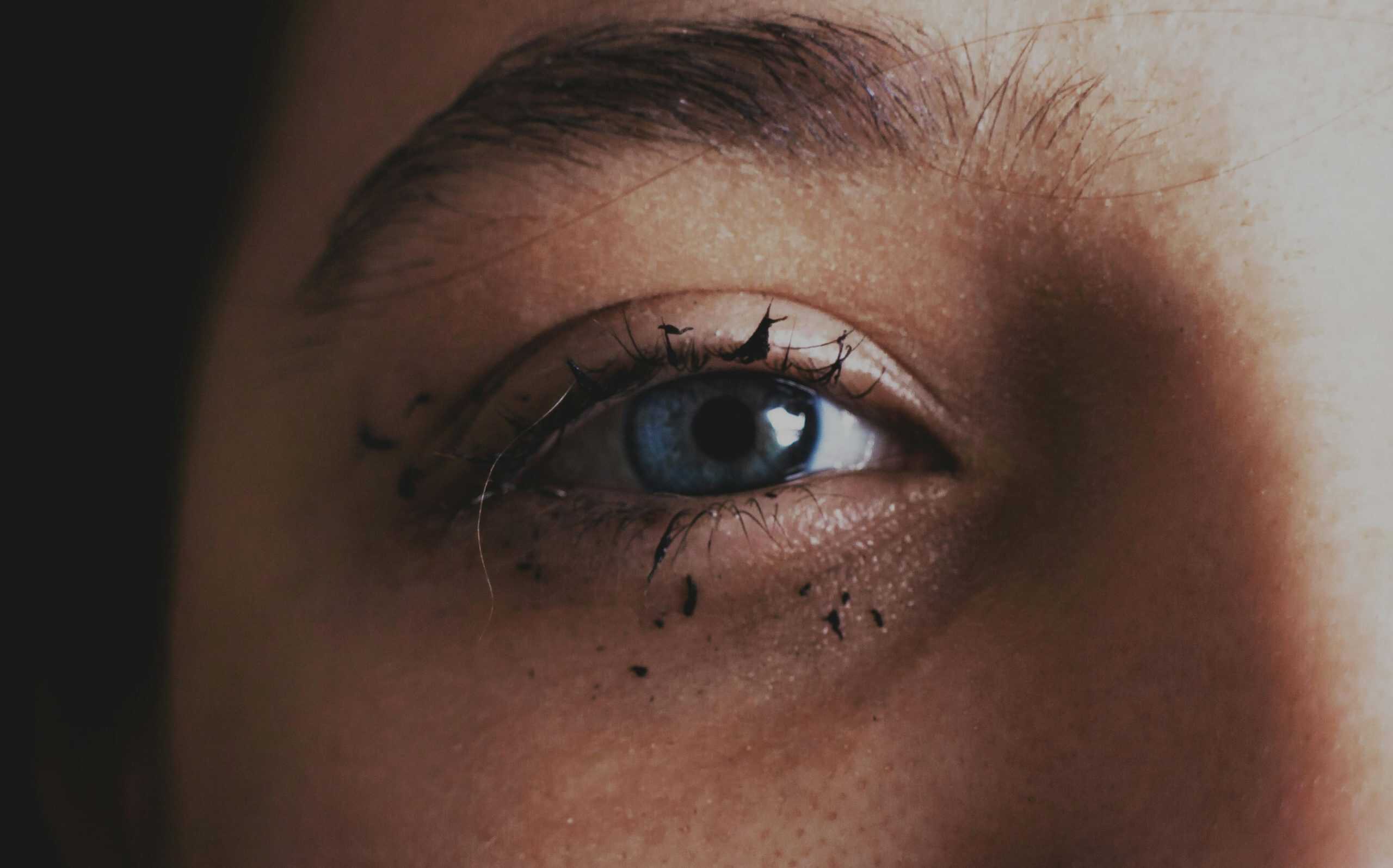 Detailed close-up of a blue eye with smeared mascara, capturing raw emotion. grunge makeup smudged