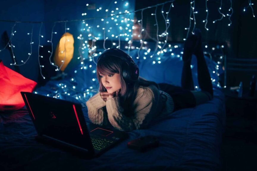 bed styling, A young woman in a cozy room, wearing headphones and using a laptop, surrounded by warm fairy lights.