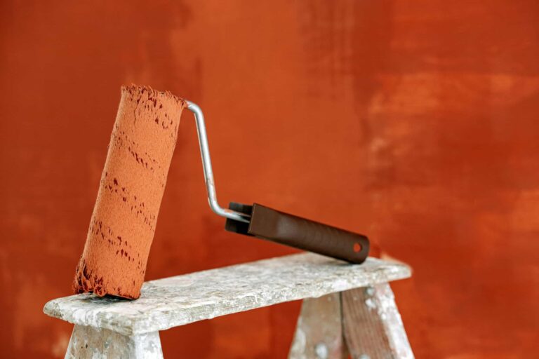 Glidden, Detailed image of a paint roller resting on a ladder with a vibrant orange wall in the background.
