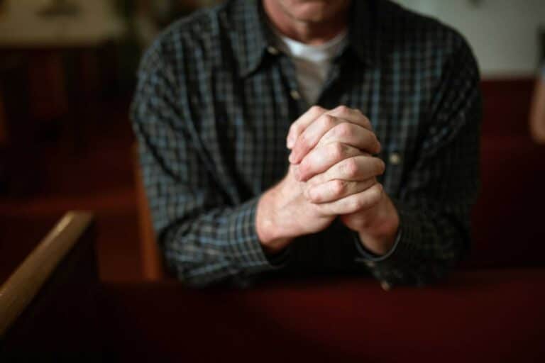 A man in a checked shirt praying in a church, hands clasped together. daily devotion