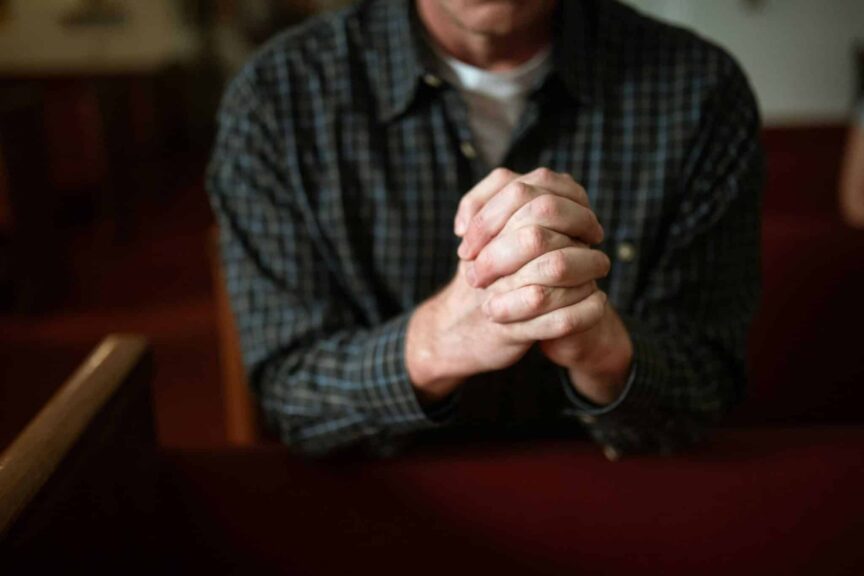 A man in a checked shirt praying in a church, hands clasped together. daily devotion