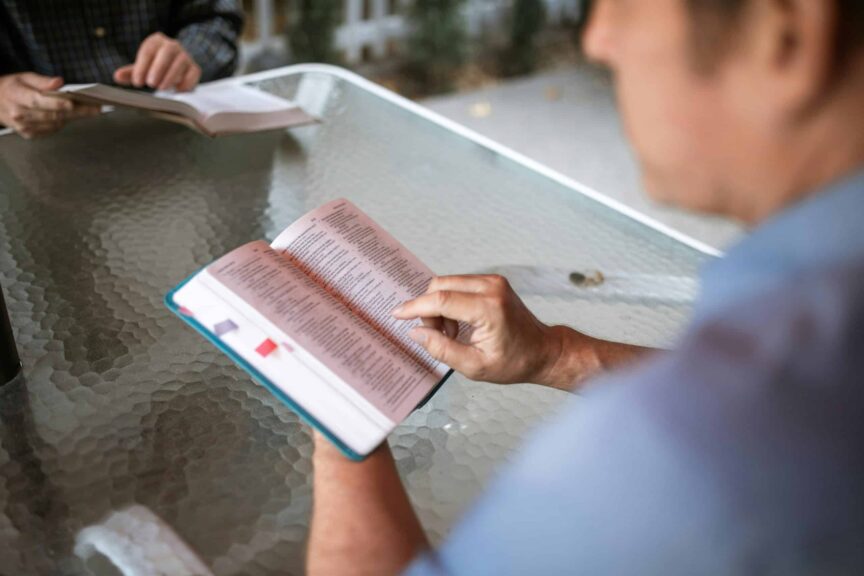 Two adults engaged in Bible study at a glass table outdoors, promoting faith and connection, and Grace