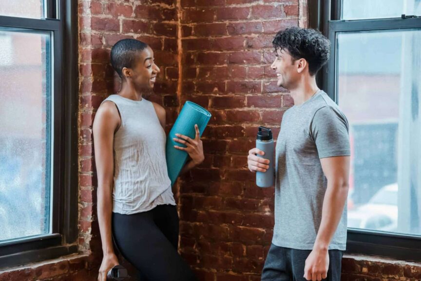 This photograph features a conversation between two people prepared for yoga class. At a gym, flirting can be a possibility between people who find connection.