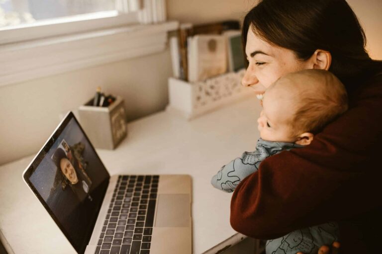 A happy mother and her baby making a video call on a laptop to connect with a long-distance loved one from home.