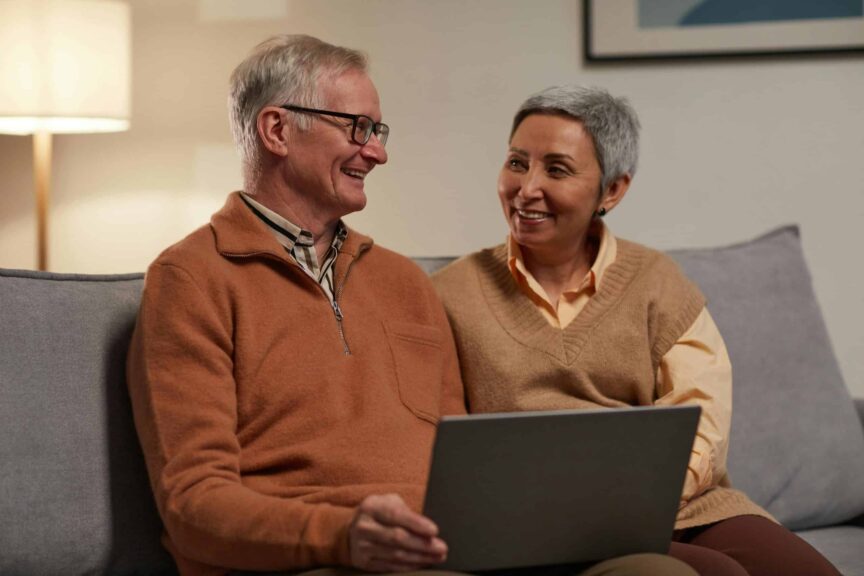 Senior couple smiling and using a laptop together in a cozy living room. Healthy patterns