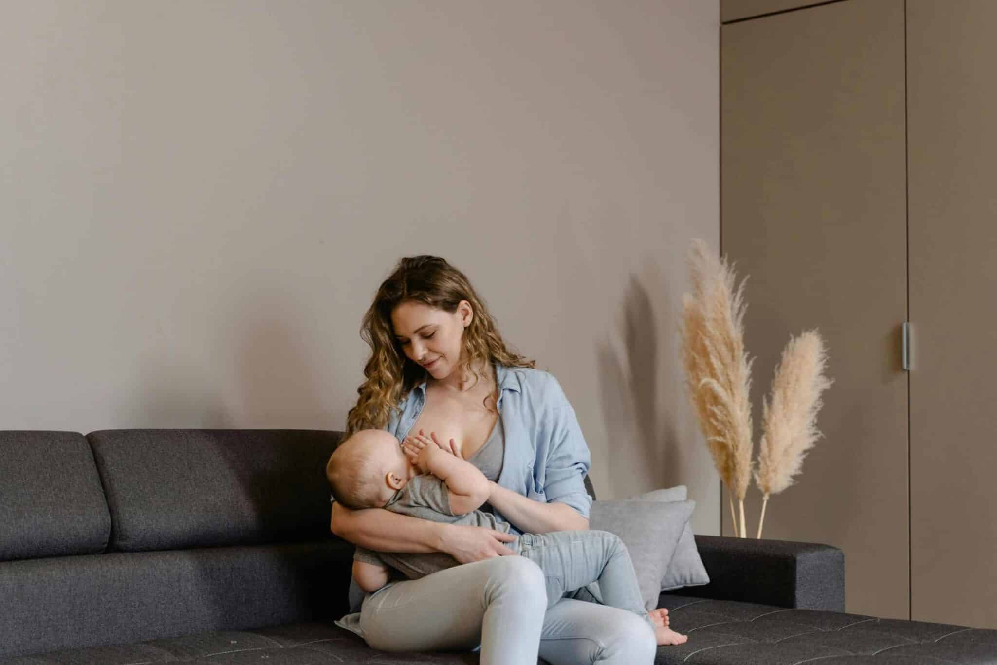 A tender moment of motherhood as a mother breastfeeds her baby on a sofa, indoors. breastfeeding