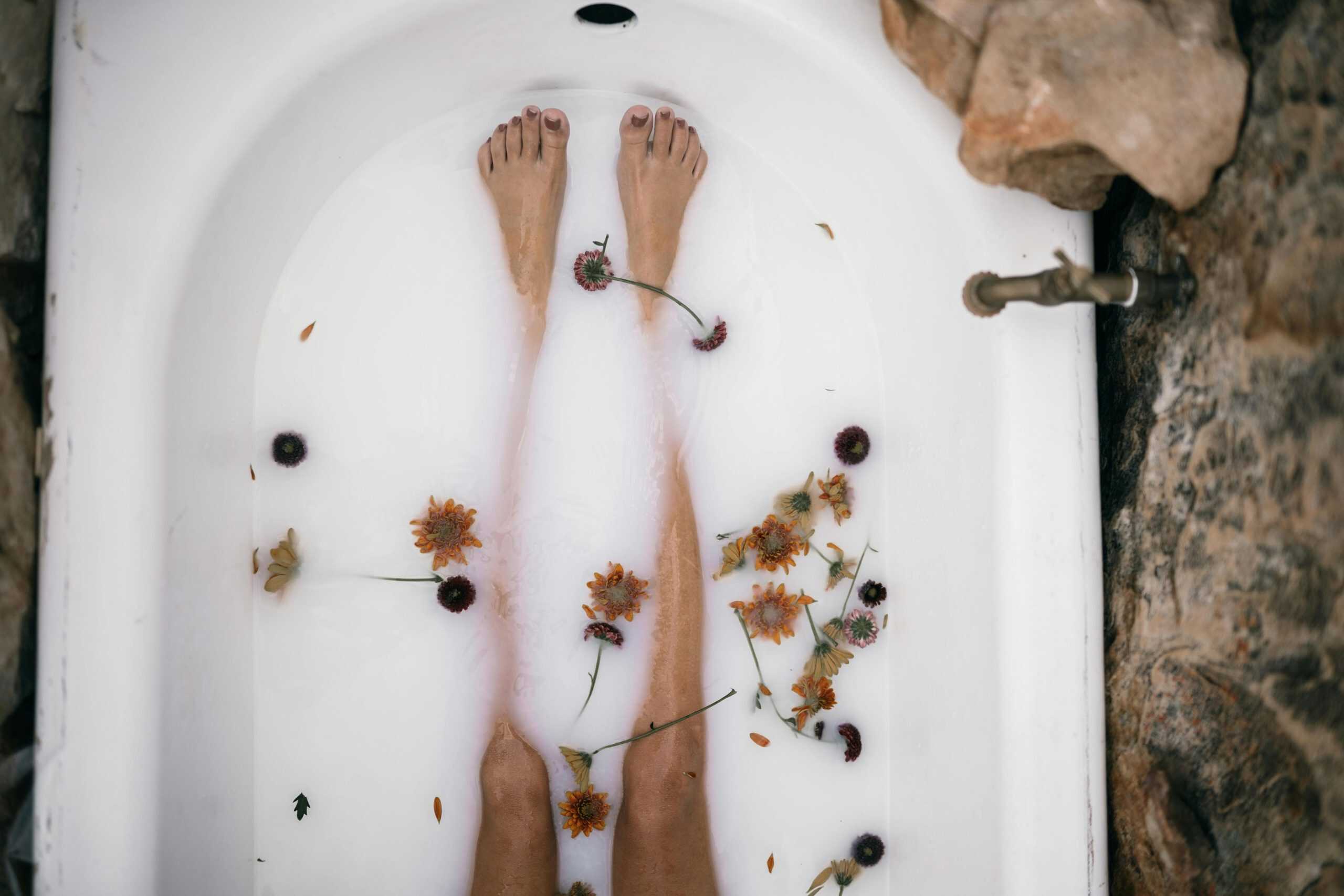 Top view of a woman's bare legs in a bathtub filled with milk and scattered flowers for a soothing bath experience. Wedding beauty ritual