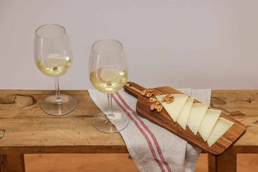 Sophisticated still life of white wine and sliced cheese with walnuts on a wooden board. Wine pairing
