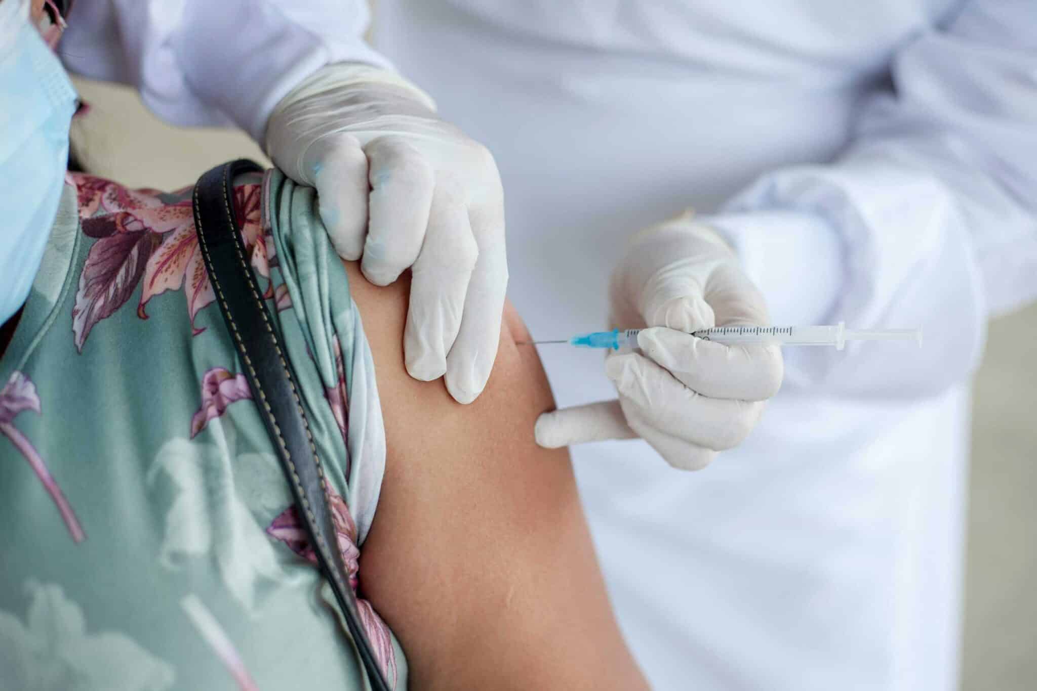 Close-up of a healthcare professional giving a vaccine shot to a patient wearing a mask. National immunization month