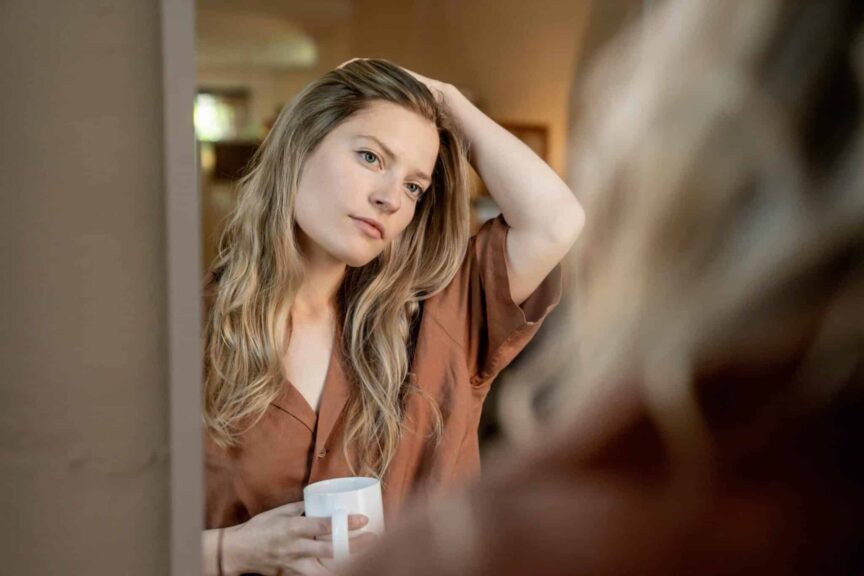 This photo is of a woman looking into a mirror and holding a coffee mug. You can check out your reflection throughout your day and use oil-blotting sheets as needed.