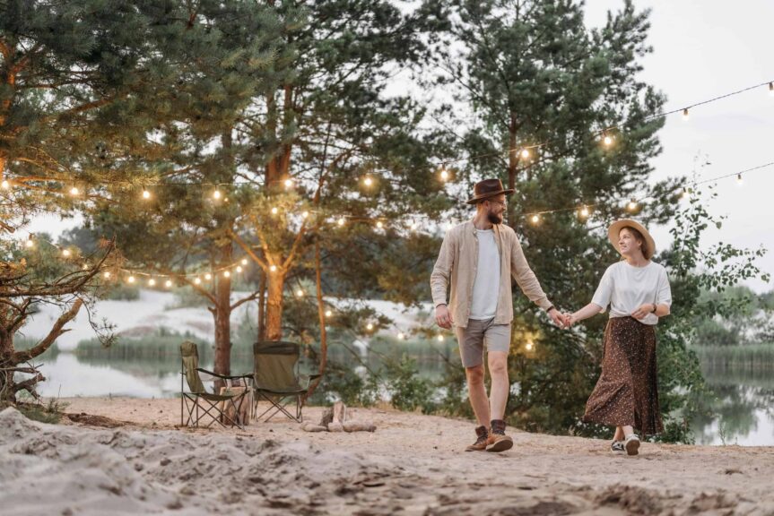 A couple strolling hand-in-hand under string lights near a serene lakeside, creating a romantic scene. intimacy retreats