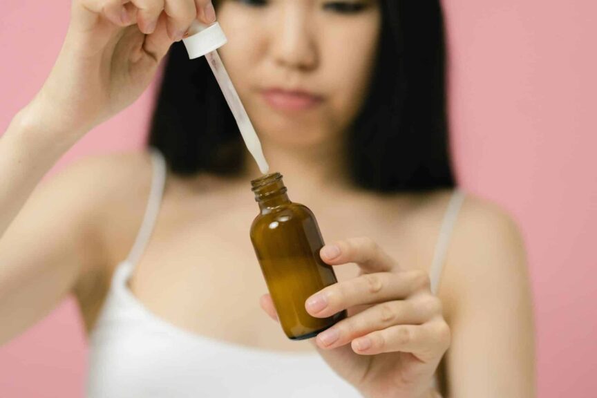 Close-up of a woman applying skincare serum with a pipette against a pink background. Hyaluronic acid