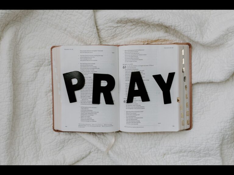 In daily devotional, an open Bible is shown with big letters spread over it that spell out PRAY. 
