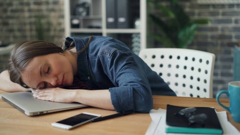 A woman laying her head on a laptop on a desk. Hashimoto's disease